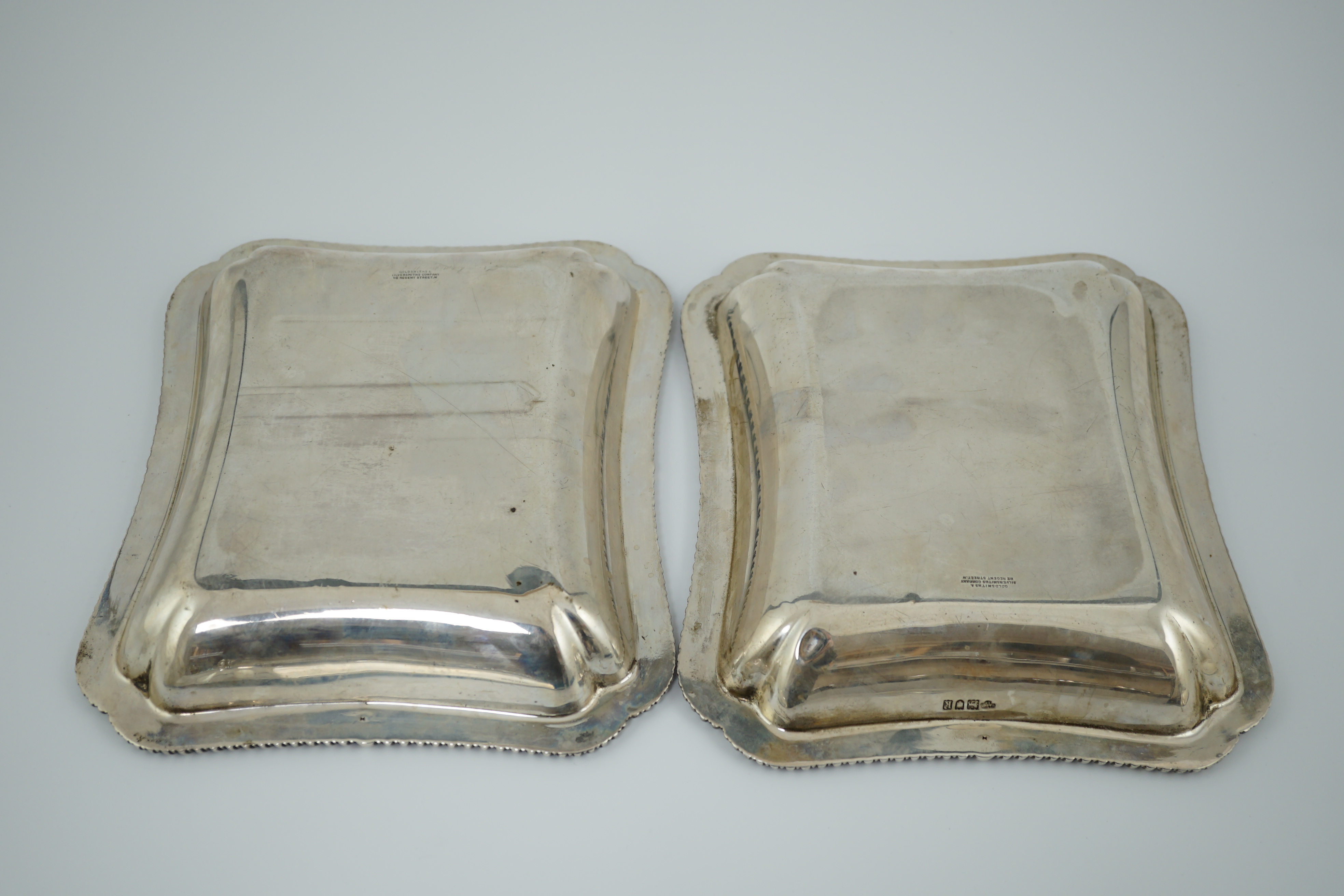 A pair of Edwardian silver shaped rectangular entrée dishes and covers with handles, by Goldsmiths & Silversmiths Co Ltd